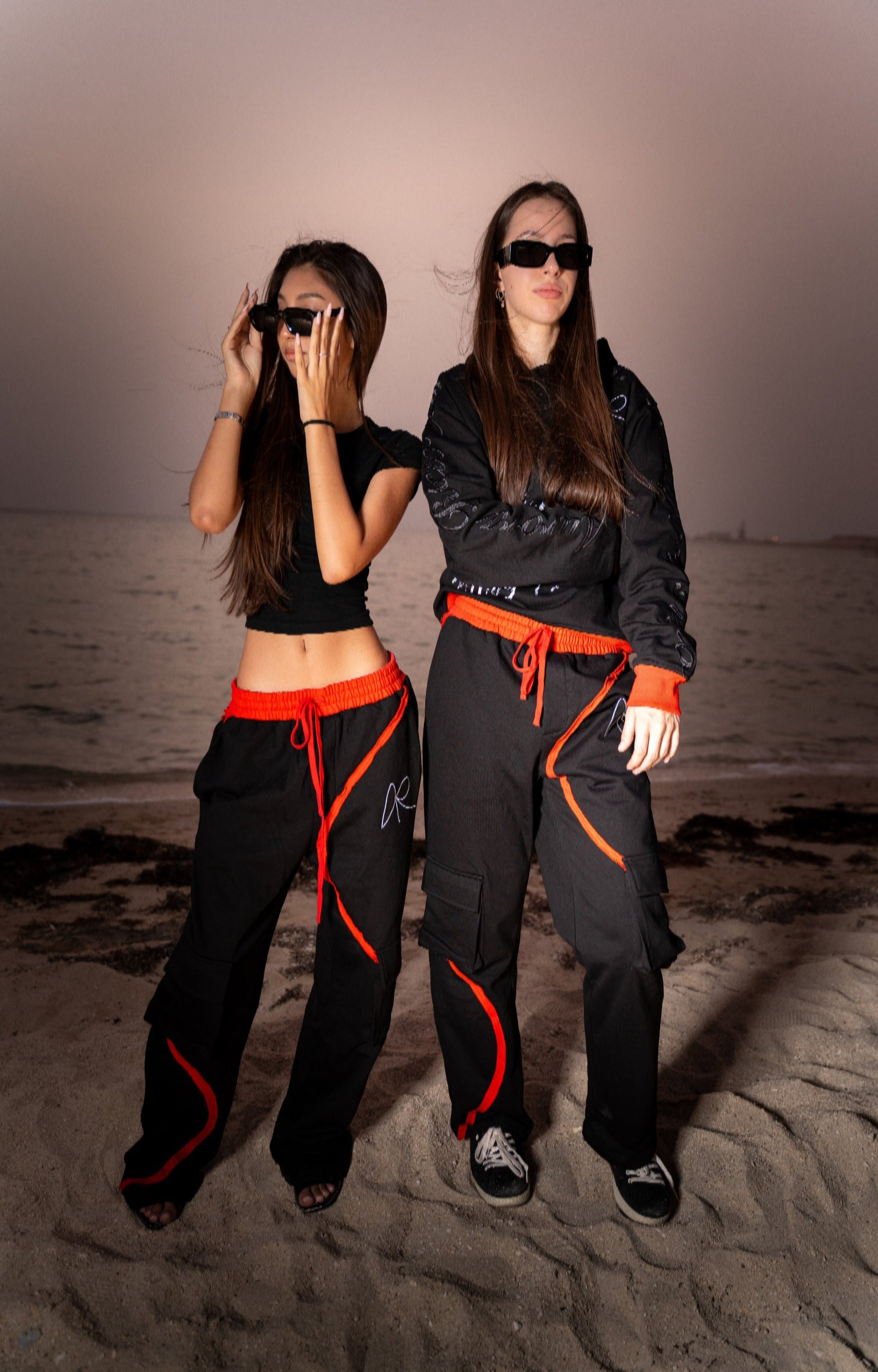 Two women in matching black outfits with red accents standing on a beach.